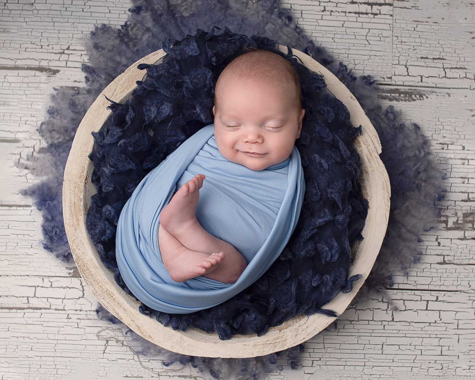 smiling newborn wrapped in blue swaddle with custom tool backdrop 