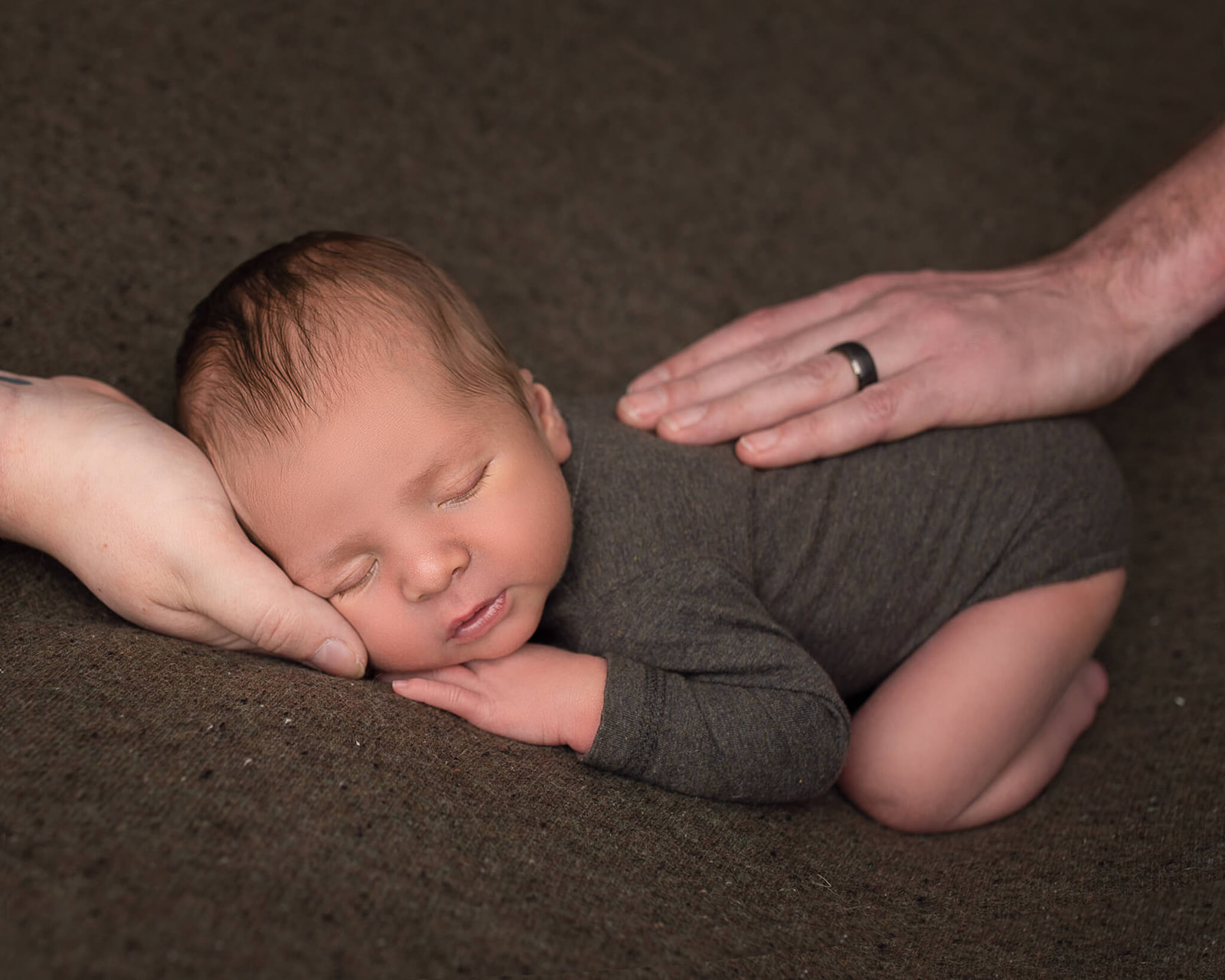 Sleeping newborn during newborn photography session in Akron, OH with parents hands on back