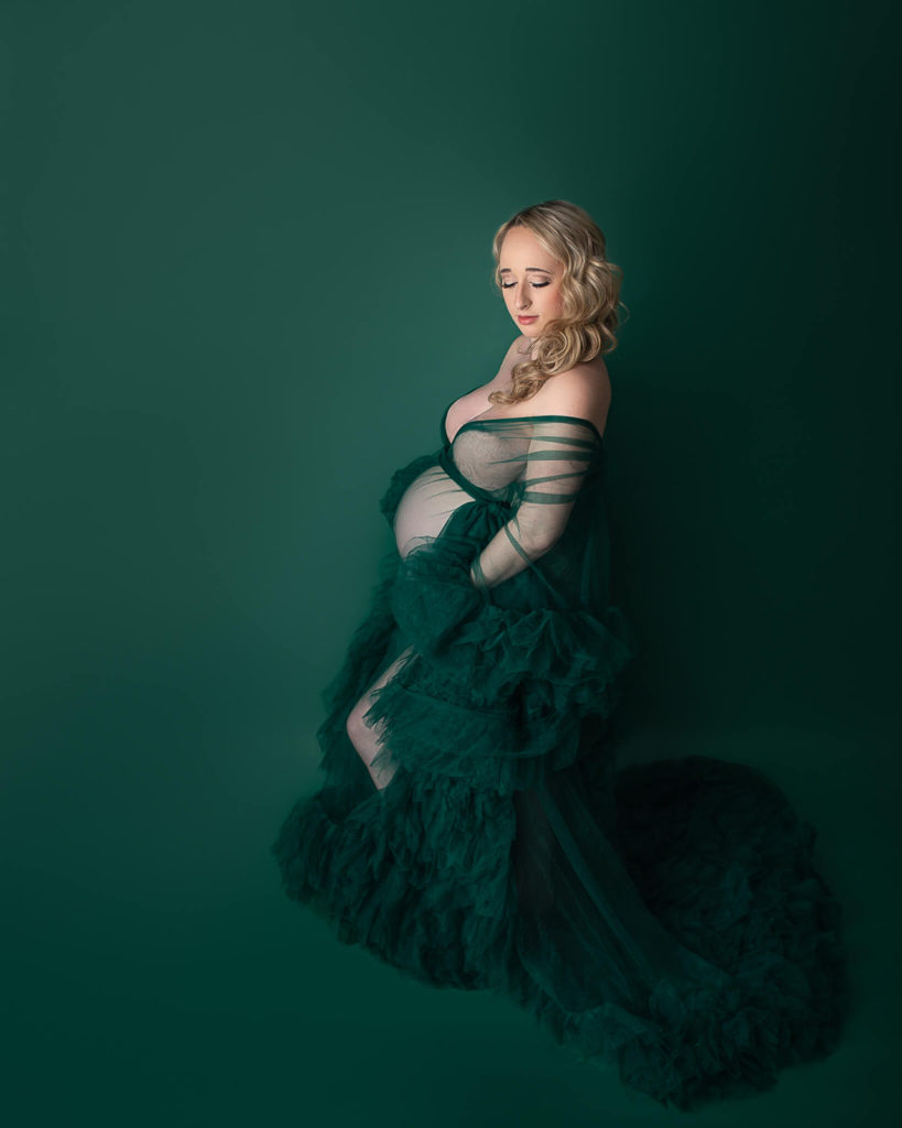 pregnant mother in green mesh gown with green background indoors during maternity photoshoot in Akron OH
