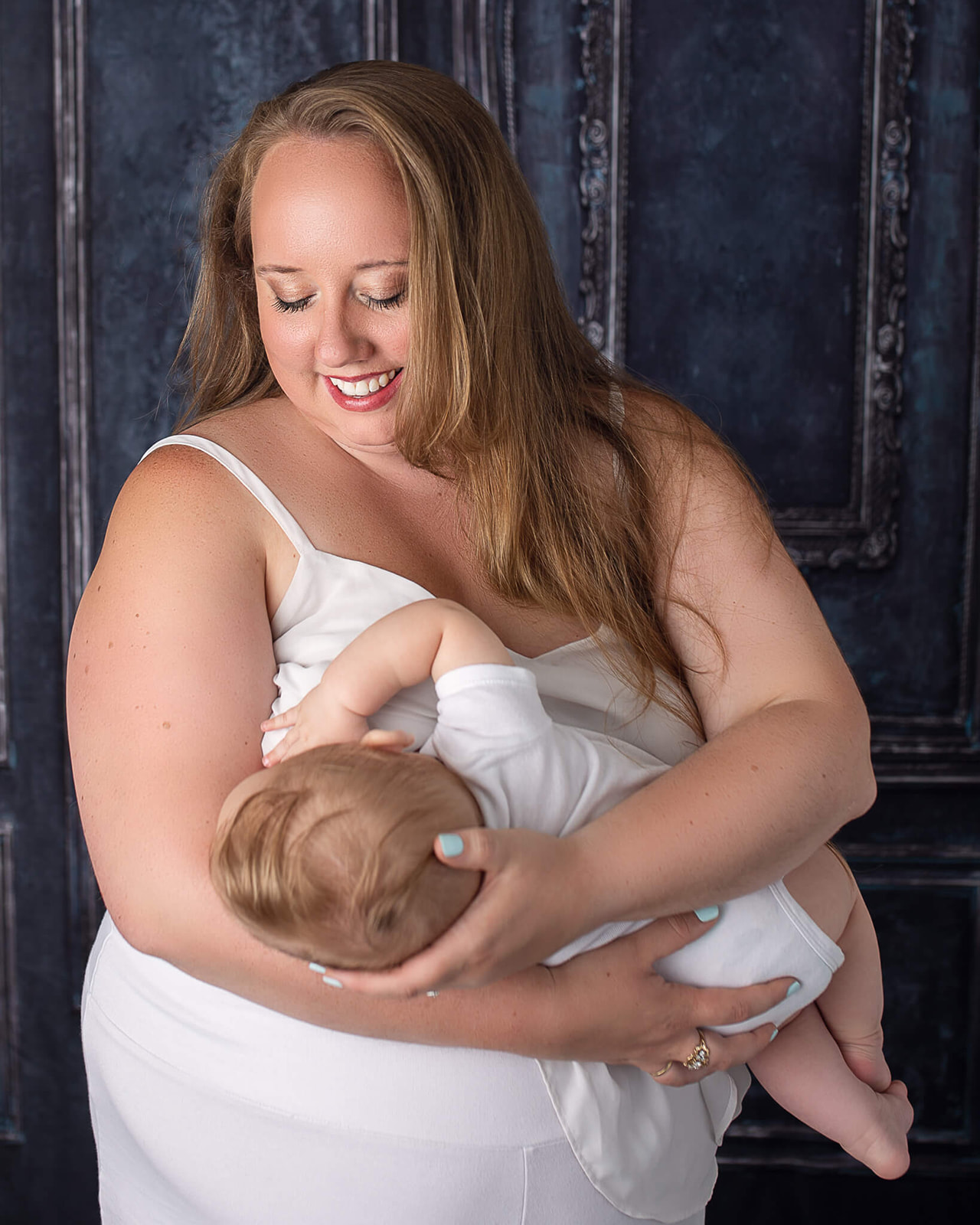 blonde mom in white dress breastfeeding little one inside during breastfeeding photoshoot in Akron, OH
