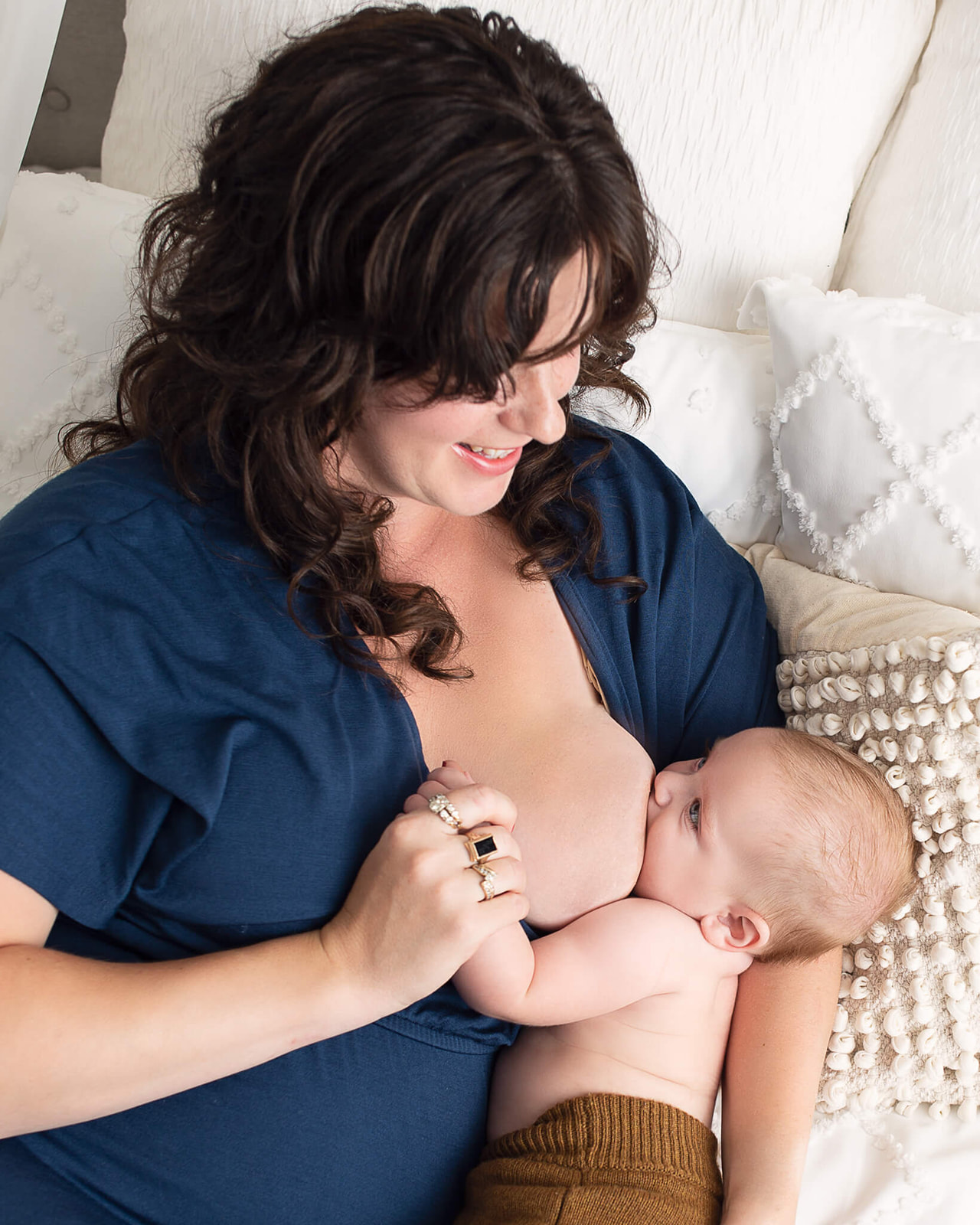 breastfeeding newborn/baby and mother in blue dress indoors on a white bed during breastfeeding photoshoot