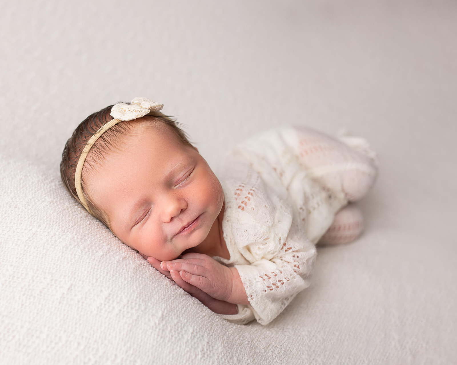 sleeping newborn with praying hands in white outfit during newborn photography session