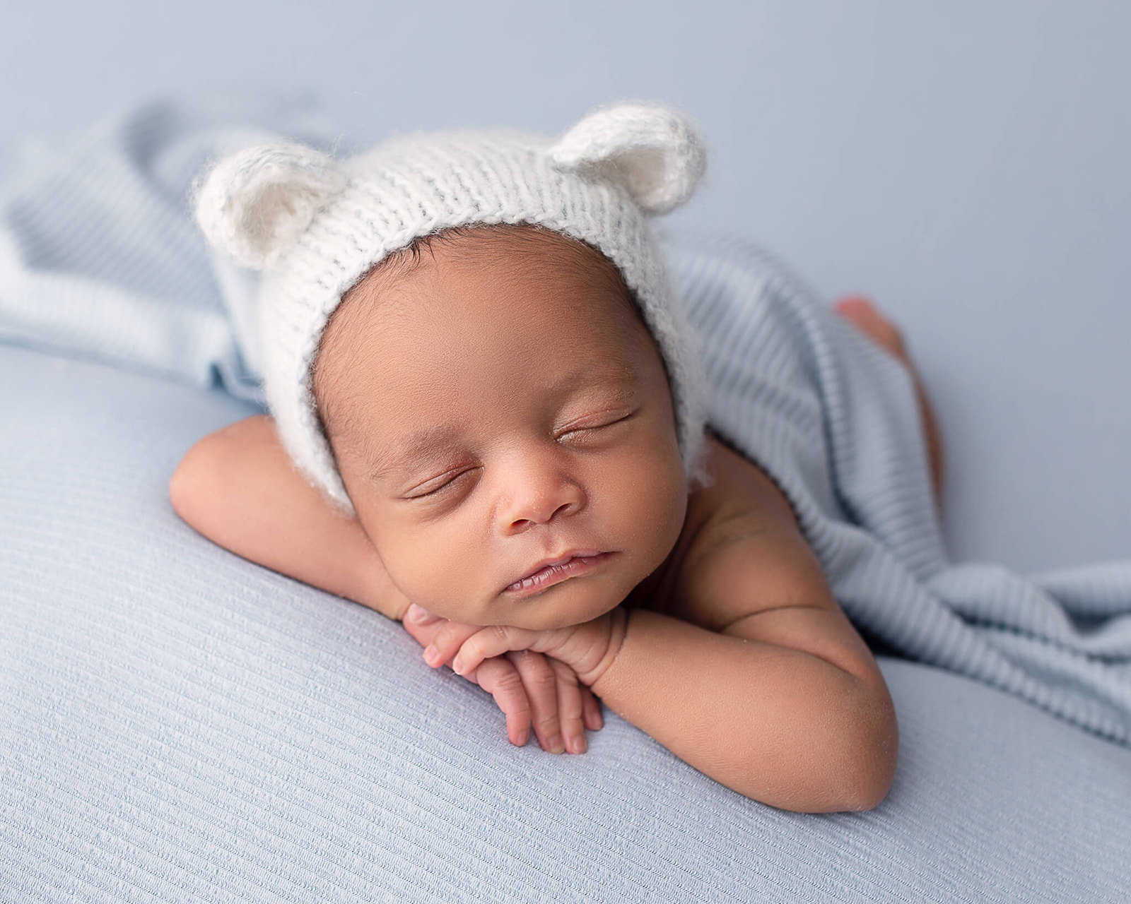 sleeping newborn during newborn photography session with white knit bear hat on head and blue blanket
