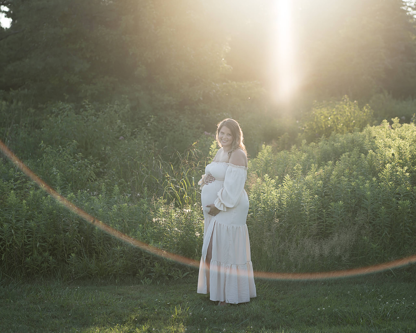 pregnant mother in white gown outside with bushes in background during maternity photo session in Akron, OH