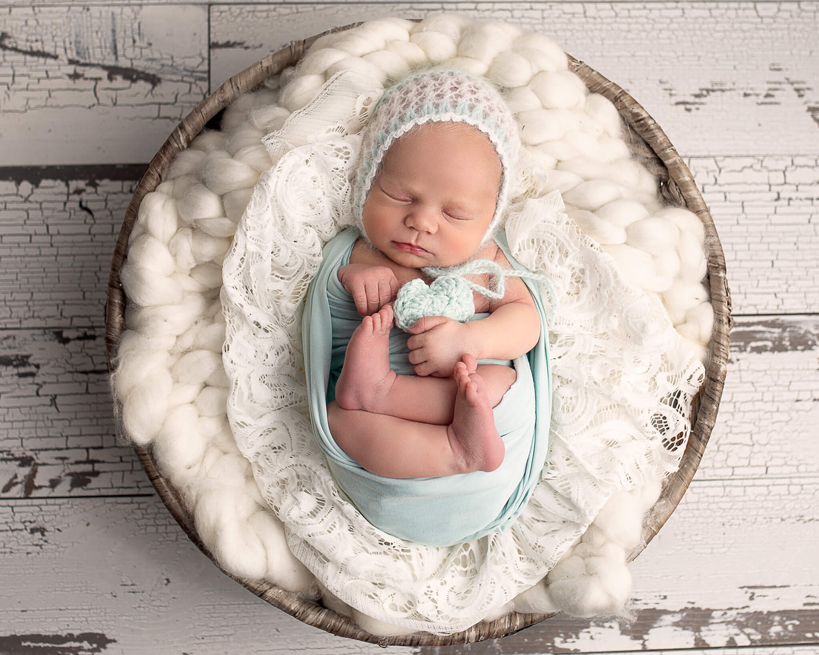 newborn in mint green wrap with knitted hat on a white blanket for best doulas in Akron OH article