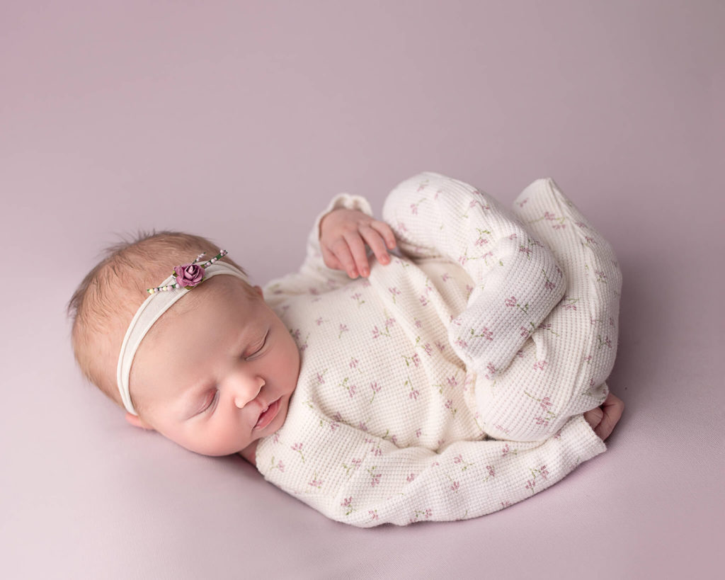 newborn in a cream onesie with small purple flowers and headband for best doulas in Akron OH article
