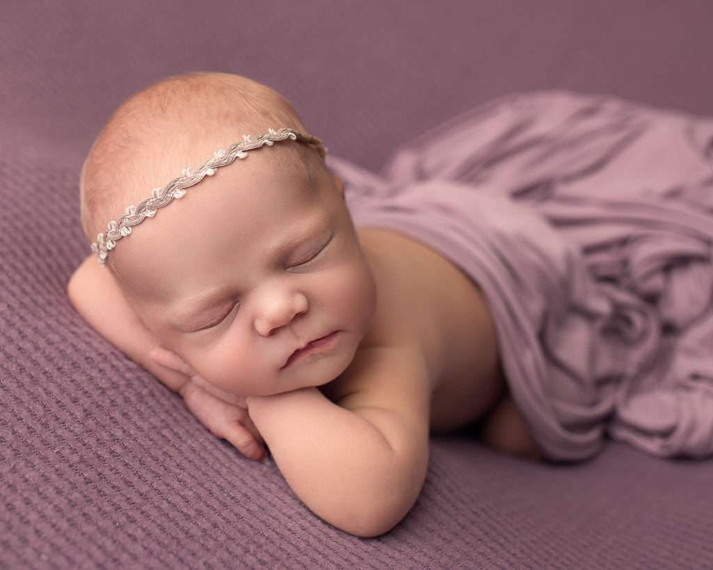 sleeping newborn with purple sheet on them and gold headband
