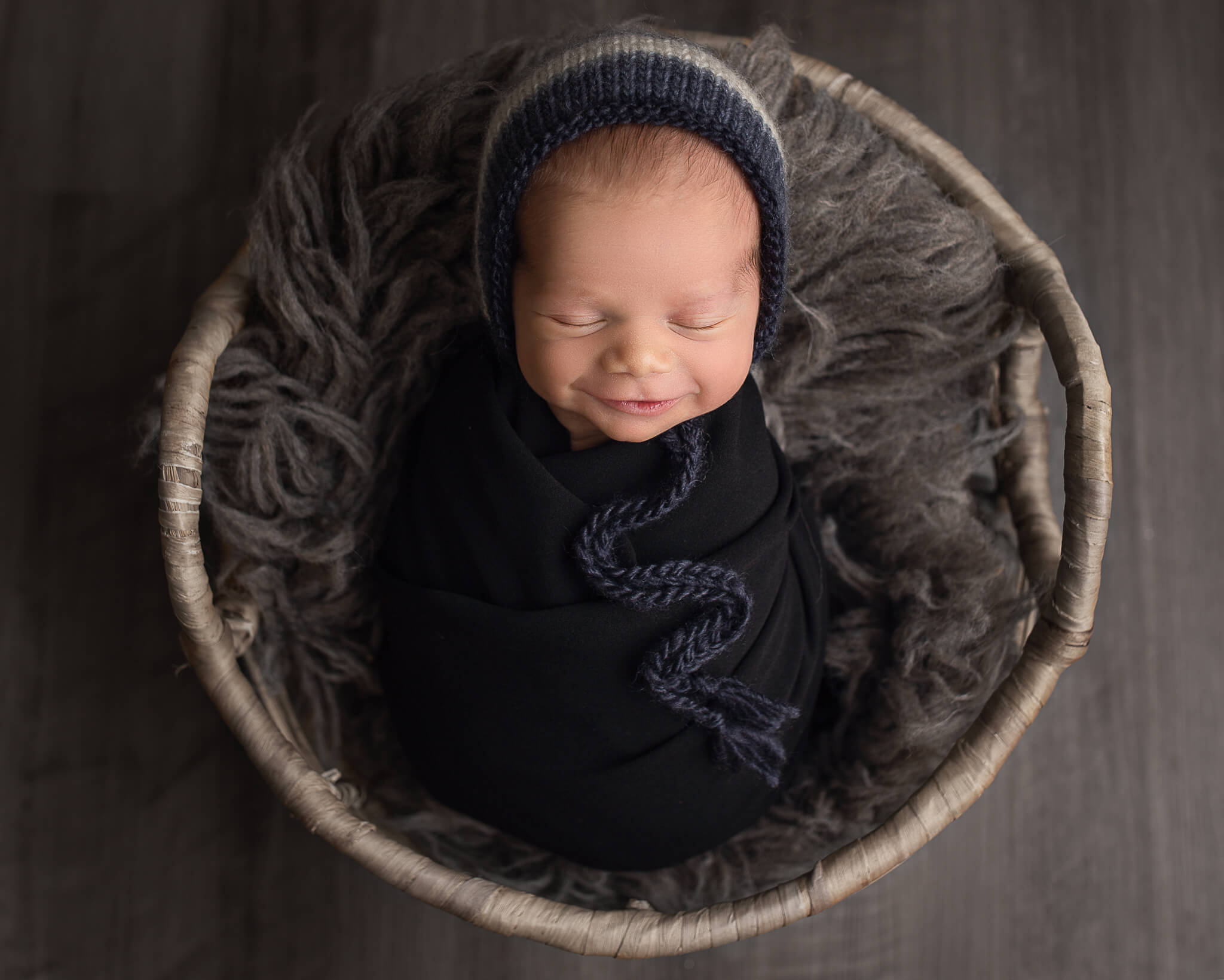 cold symptoms in babies in blog photo of sleepy, smiling baby in a basket with fur blanket and black blanket