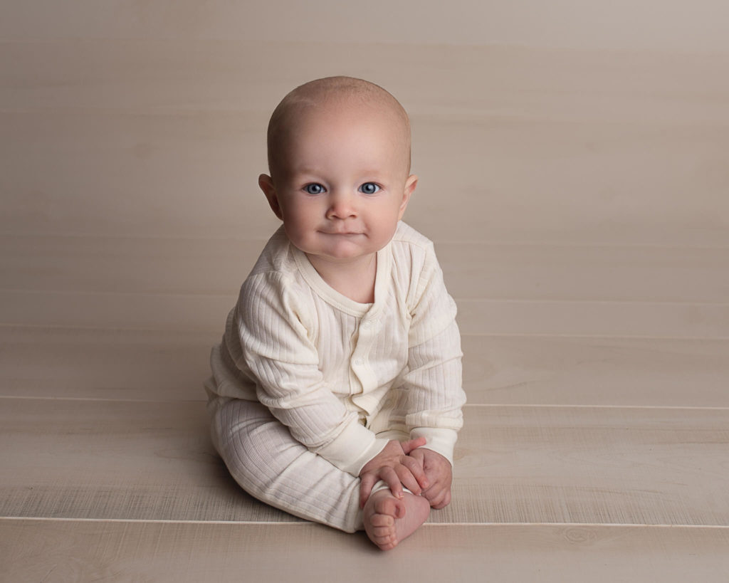 how to get your newborn to latch for feedings in blog photo of young baby sitting up in white onesie
