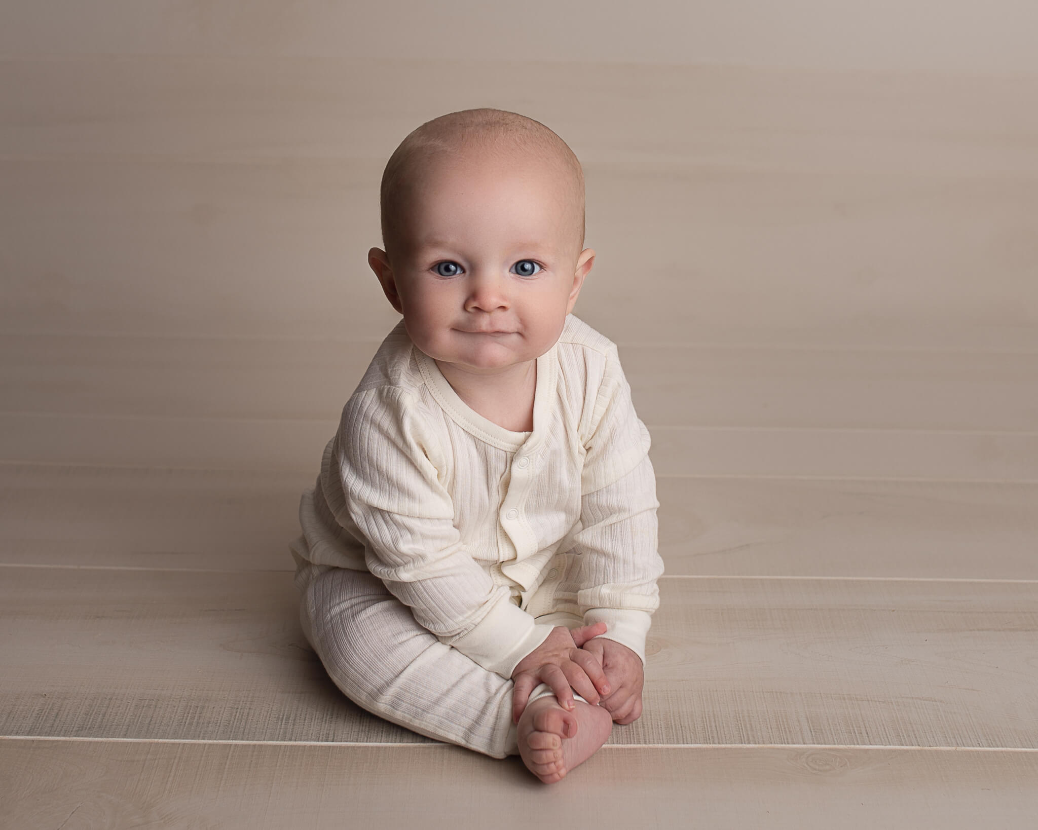 best types of clothing fabric for newborns in blog photo of baby sitting up in a cream colored onesie