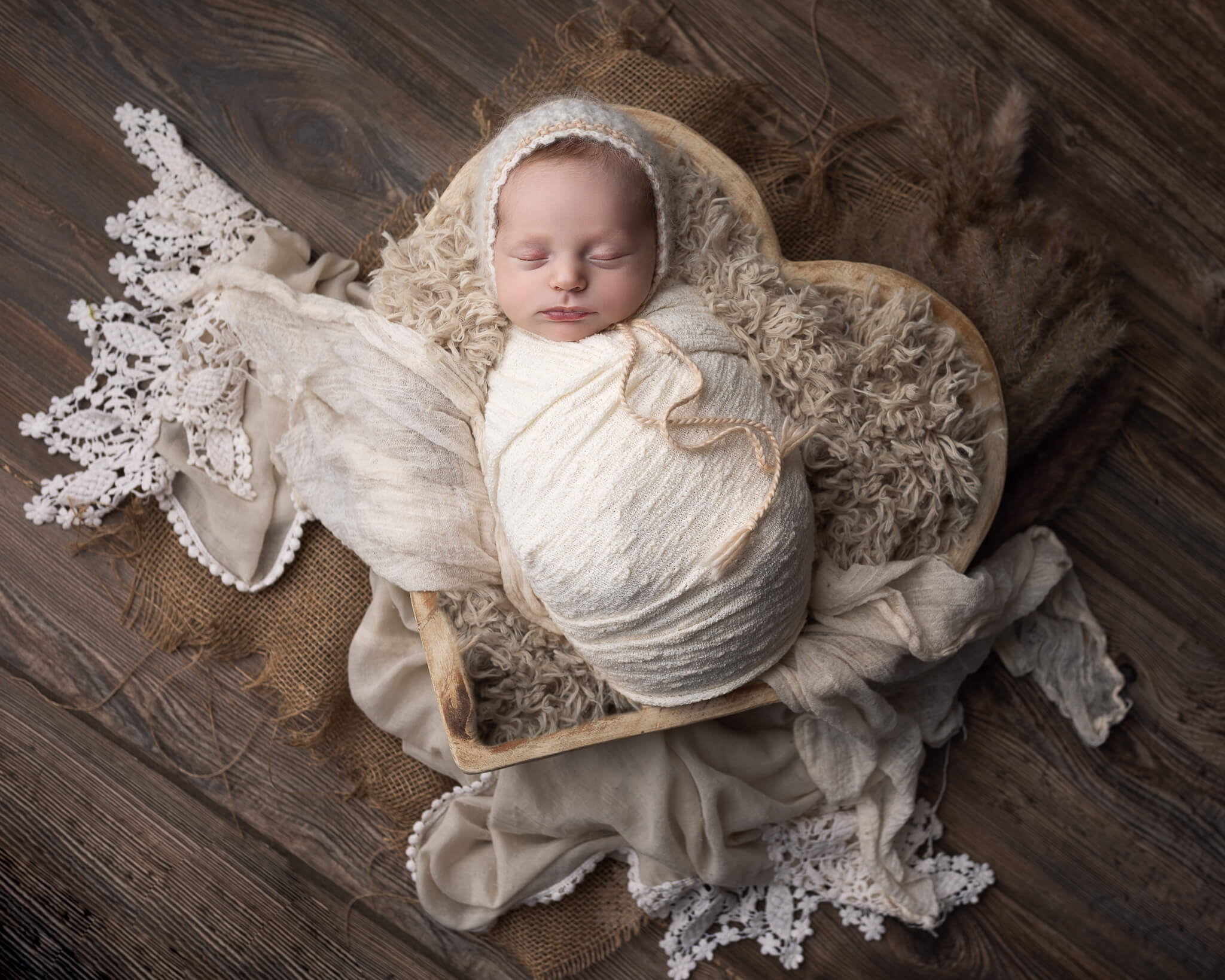 benefits of infant and newborn massage  in blog photo of sleeping newborn in white swaddle in heart basket