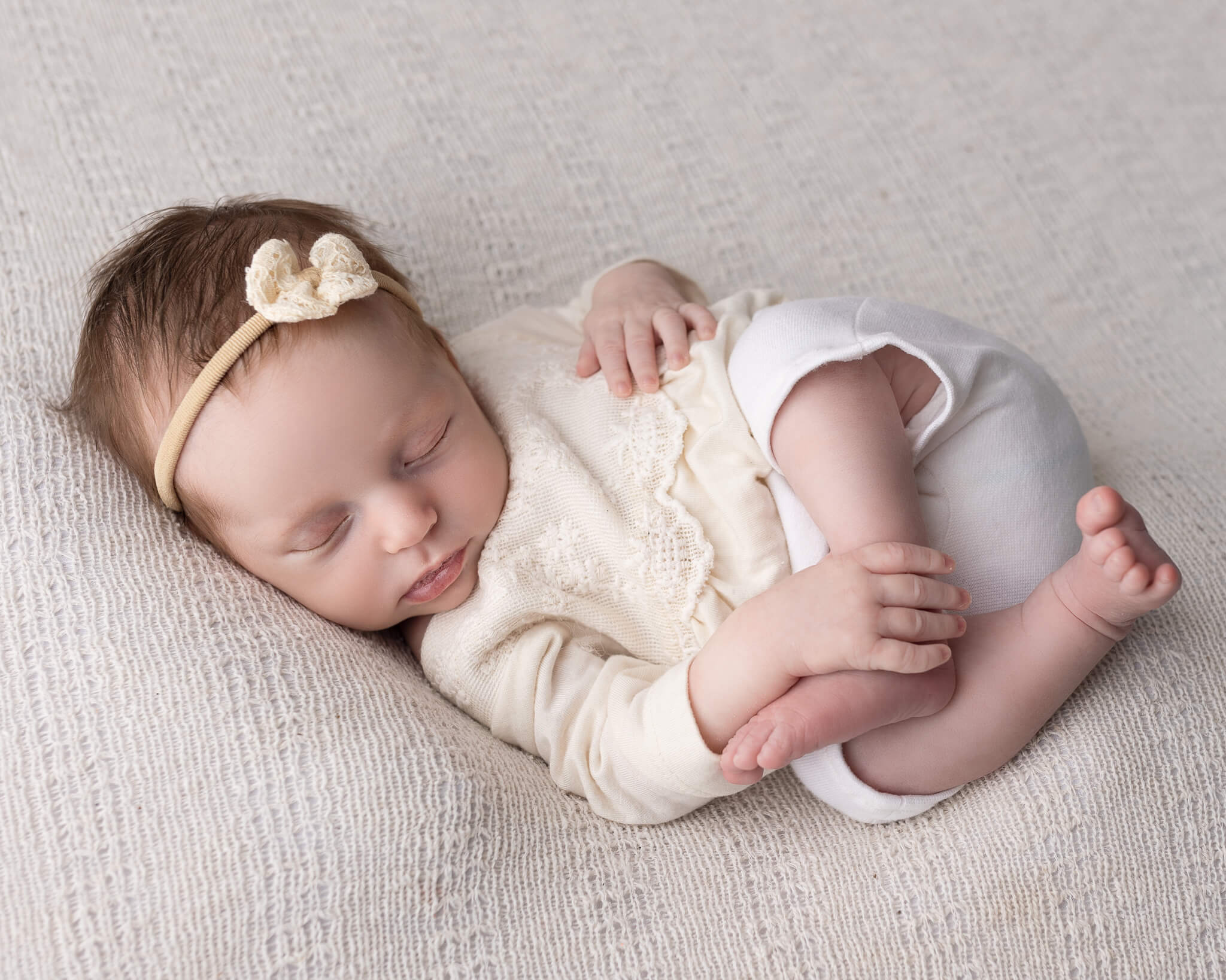 benefits of infant and newborn massage  in blog photo sleeping newborn girl in white outfit on white blanket