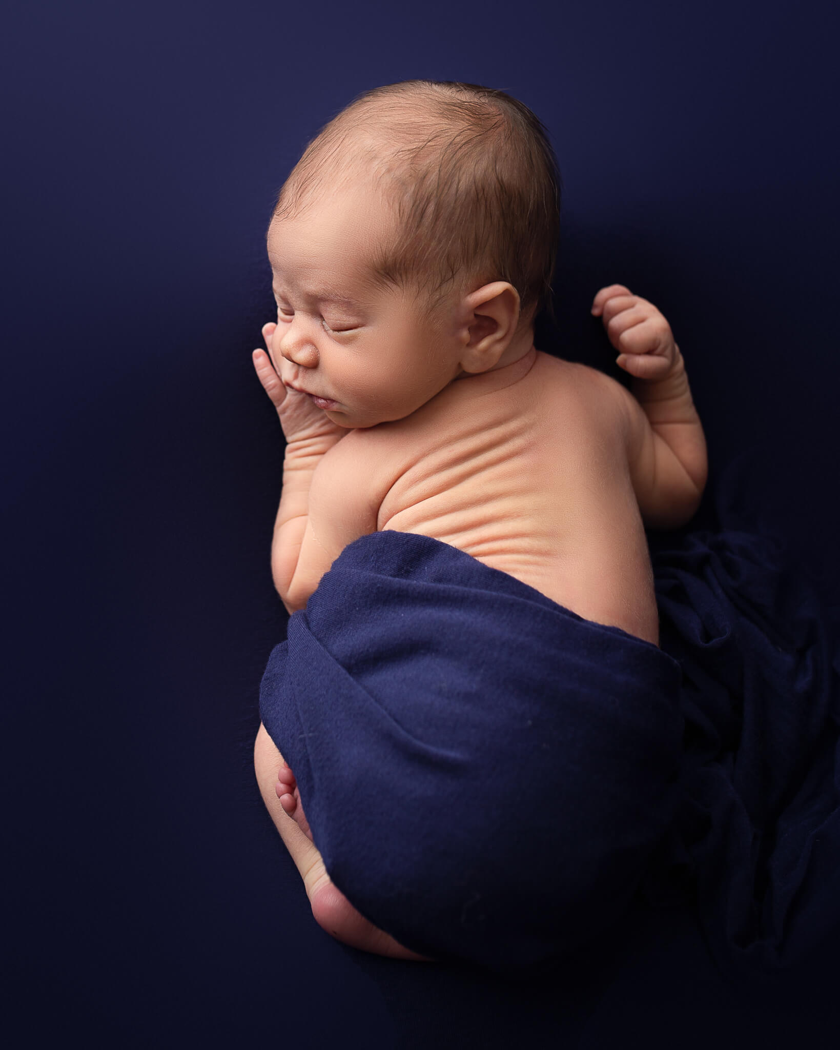 benefits of infant and newborn massage in blog photo of sleeping newborn in navy blue blanket