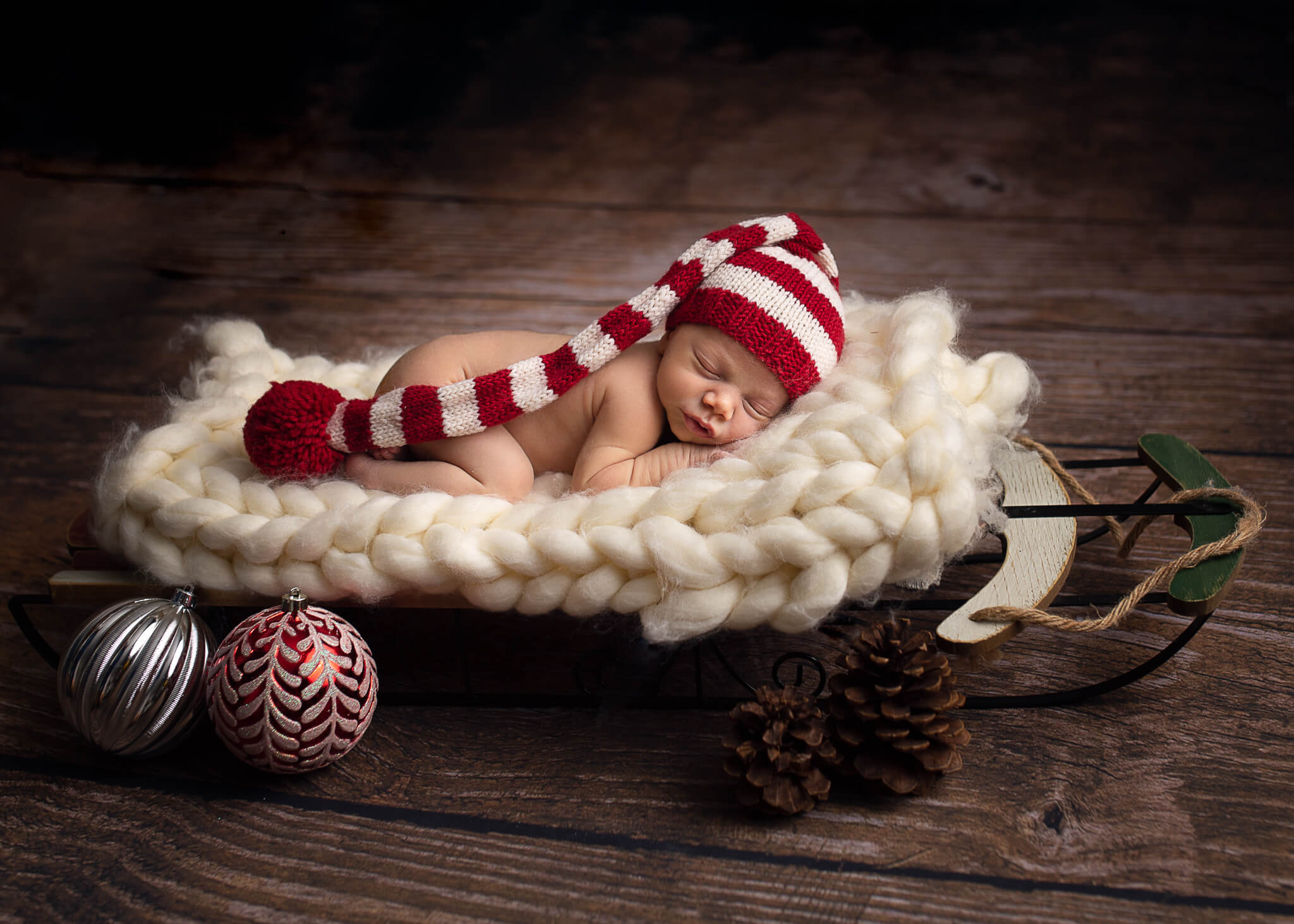 guide to newborn care in blog photo of newborn laying in a winter sleigh on fluffy white blanket with striped hat