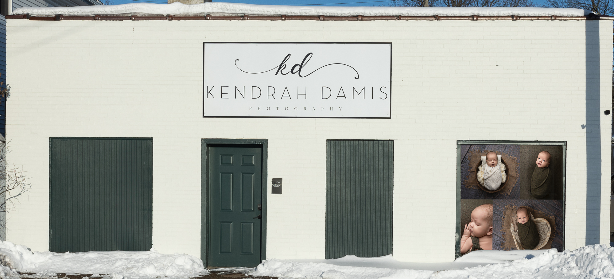 Exterior of Kendrah Damis Photography studio building with newborn portrait display in the window on a snowy day