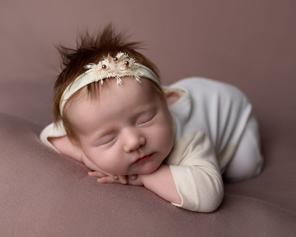 Akron newborn photography portrait of a sleeping newborn posed on soft mauve fabric wearing a delicate floral headband