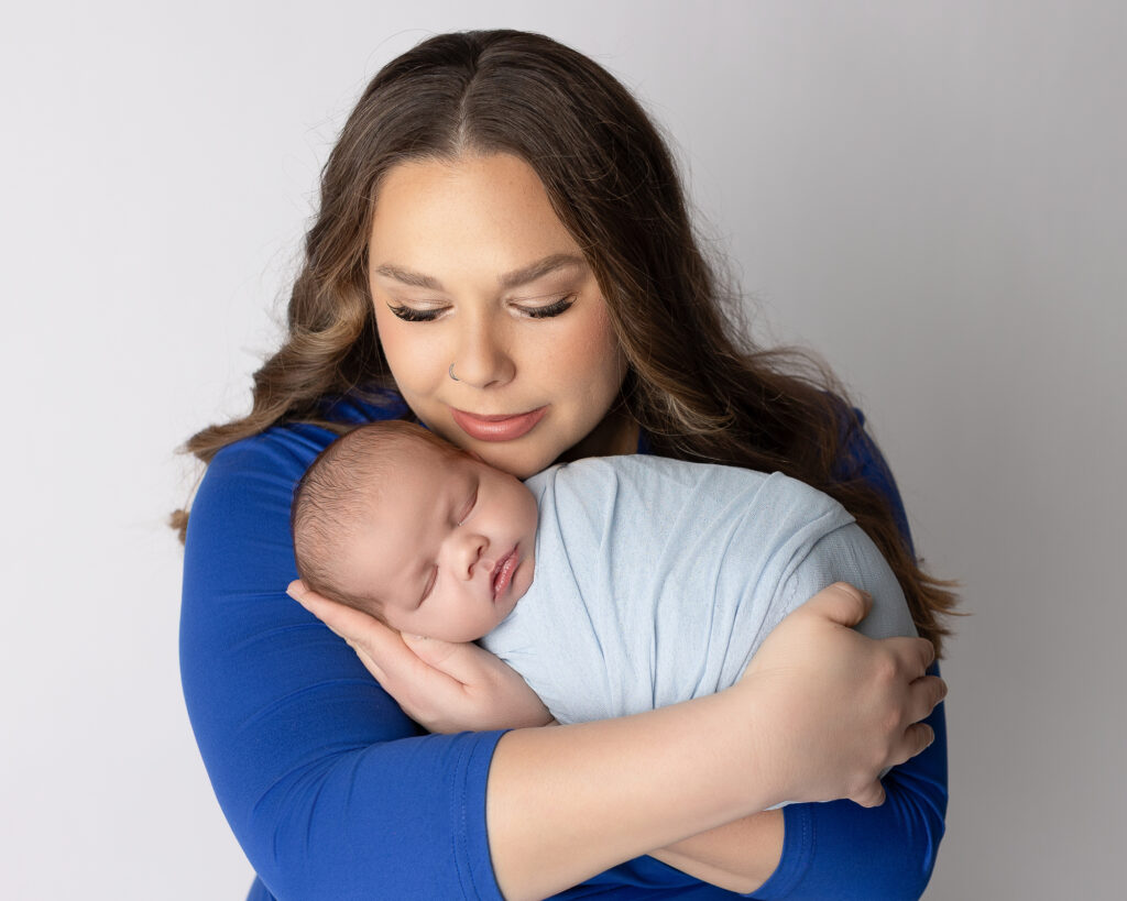 Mother gently holding her sleeping newborn wrapped in a soft blue blanket during Akron newborn photography session