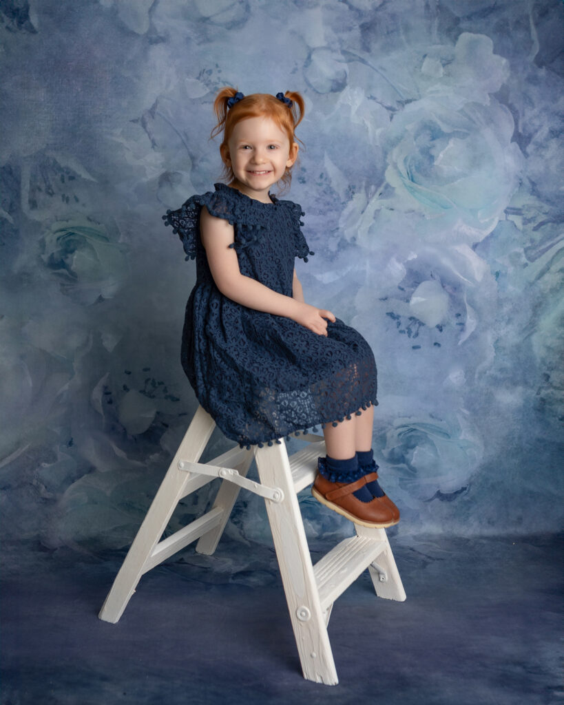 Toddler girl sitting on a small white ladder during a milestone photo session, a fun activity for toddlers in Canton Ohio.