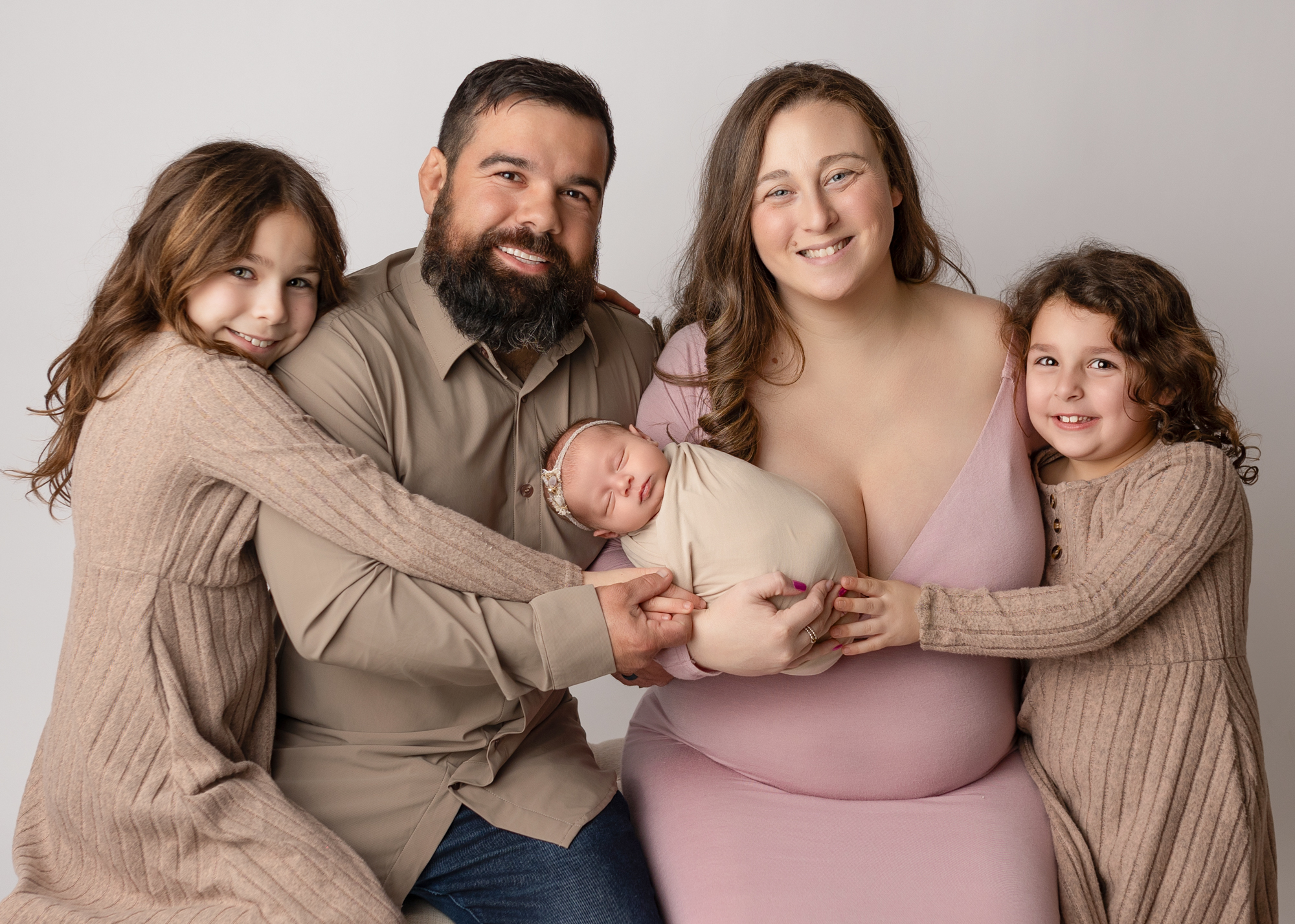 Family newborn portrait with parents and two sisters wearing coordinated neutral outfits while holding their newborn baby