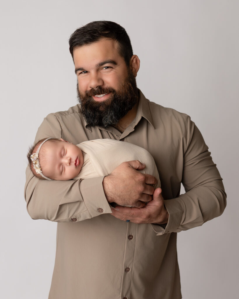 dad holding newborn baby wearing neutral tan shirt during newborn photography session